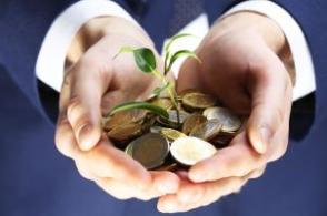 image shows two hands holding coins with a seedling in the centre