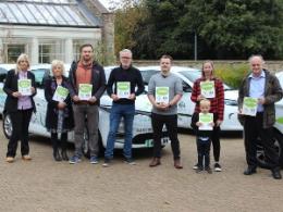 People holding certificates in front of cars