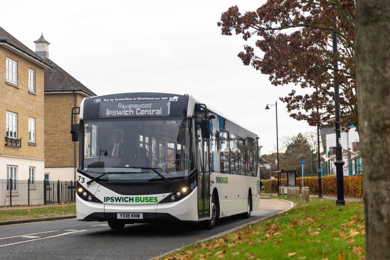 A single decker bus on a road through a residential area