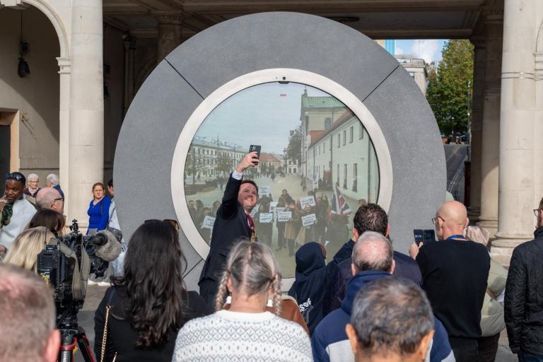A crowd of people in front of a circular Portal sculpture in Ipswich