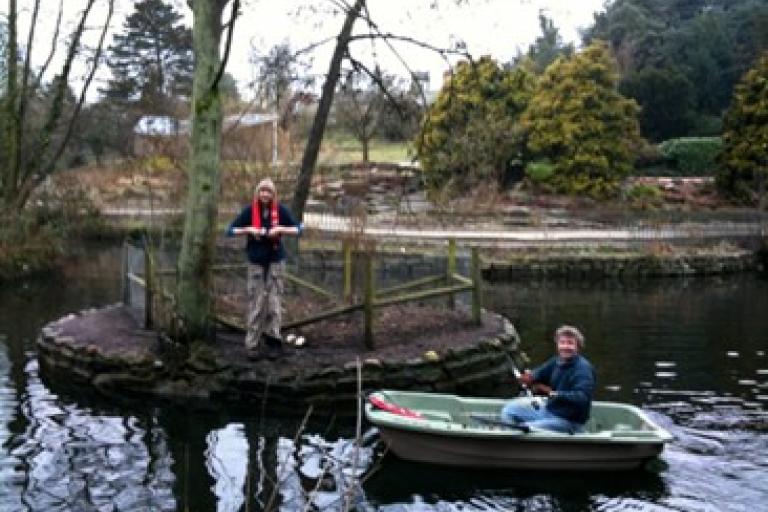 Two volunteers use a boat to work on the pond in Christchurch Park