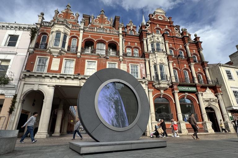 A large circular sculpture in a town centre beside historic building