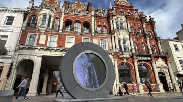 A large circular sculpture in a town centre beside historic building