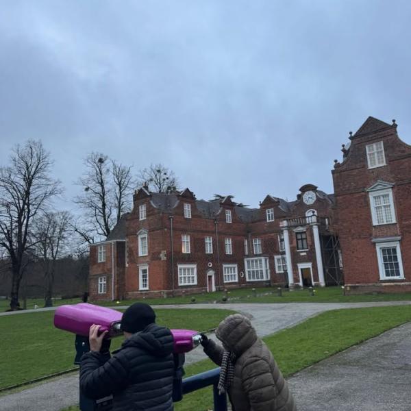 Two people looking through pink binoculars in front of Christchurch Mansion